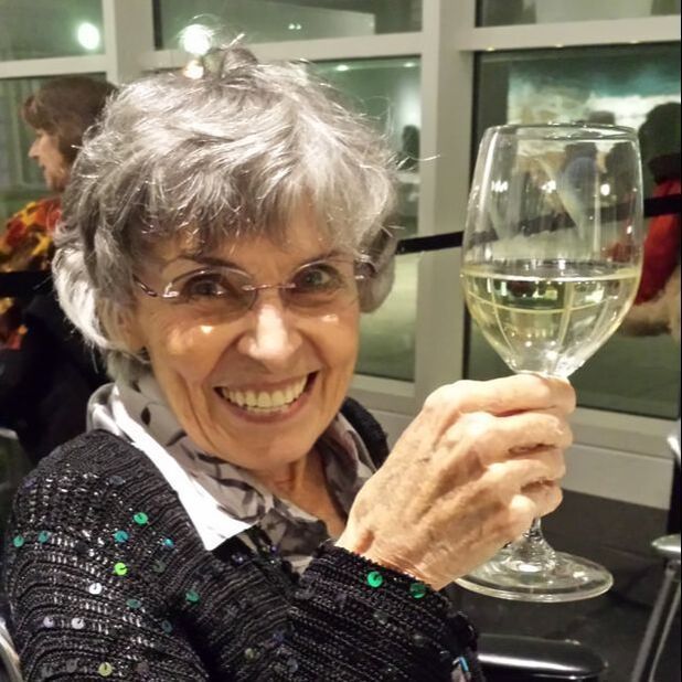 Smiling woman with gray hair holding up a glass of white wine indoors