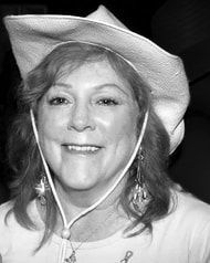 Smiling woman in a white cowboy hat and necklace, facing the camera in a black-and-white portrait