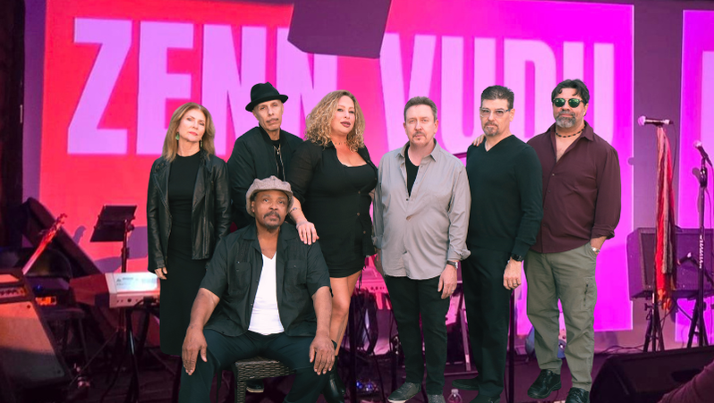 Seven people posing on a brightly lit pink stage with a large “Z” backdrop, holding musical instruments.