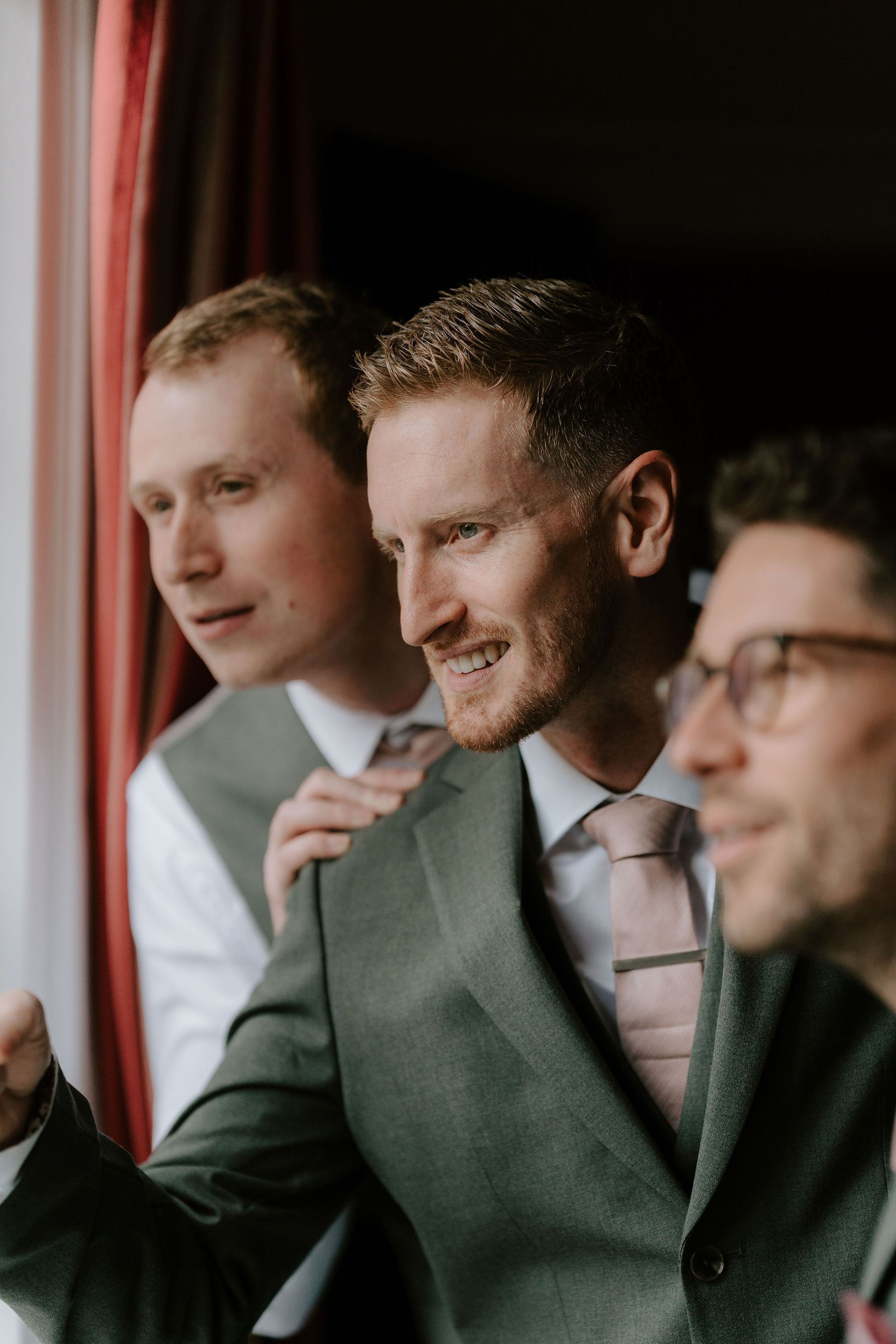 Three people in suits standing by a window, looking outside and talking