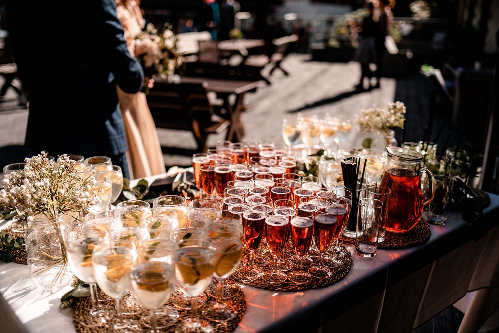 People sharing plates of food around a rustic wooden table with drinks and a centerpiece of greenery