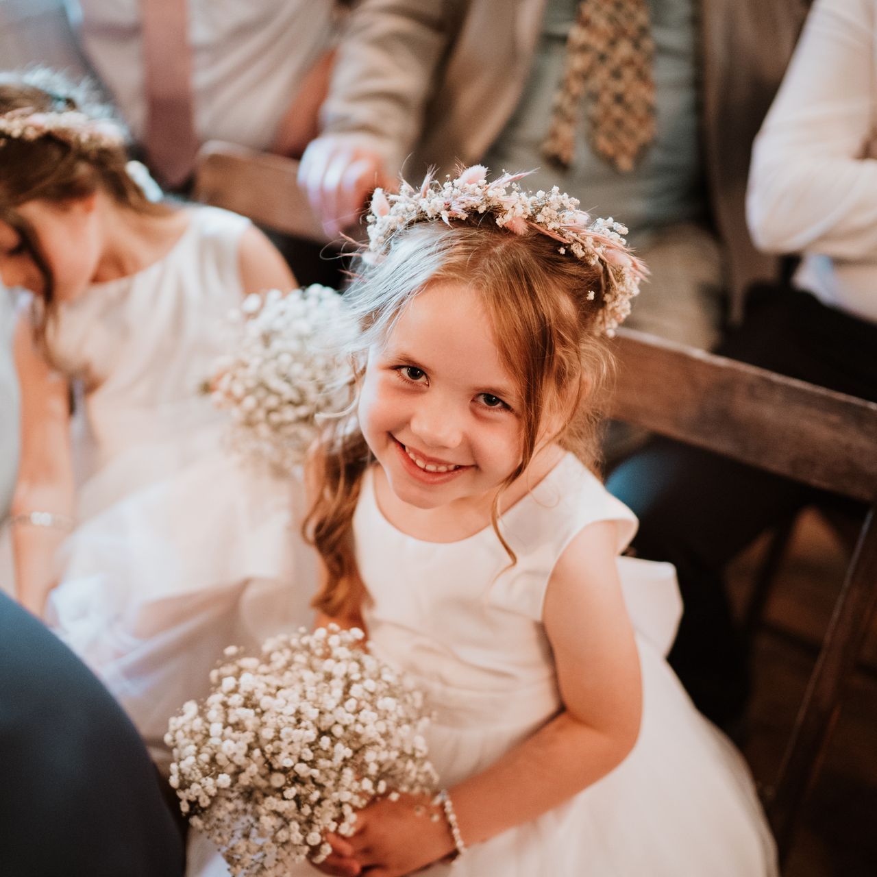 Smiling flower girl in a white dress holding a bouquet at a wedding ceremony