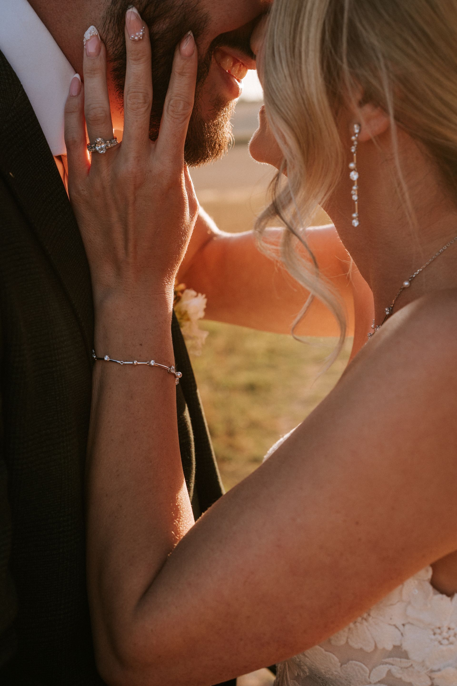 Two people embracing at sunset, with a woman’s hand on a man’s face, wearing a wedding ring.