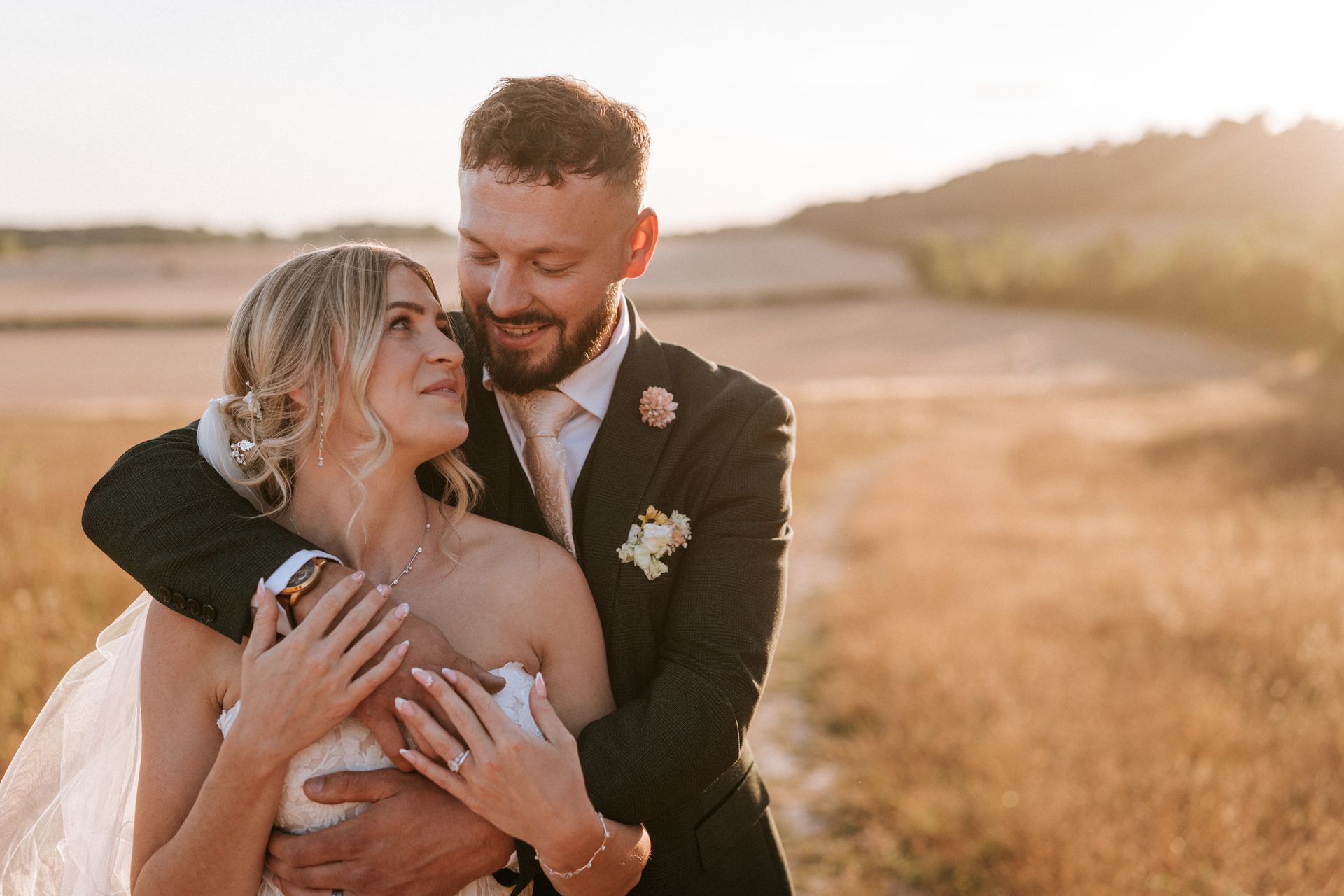 A couple holding hands walks through a sunlit field at sunset, with long shadows and warm golden light.