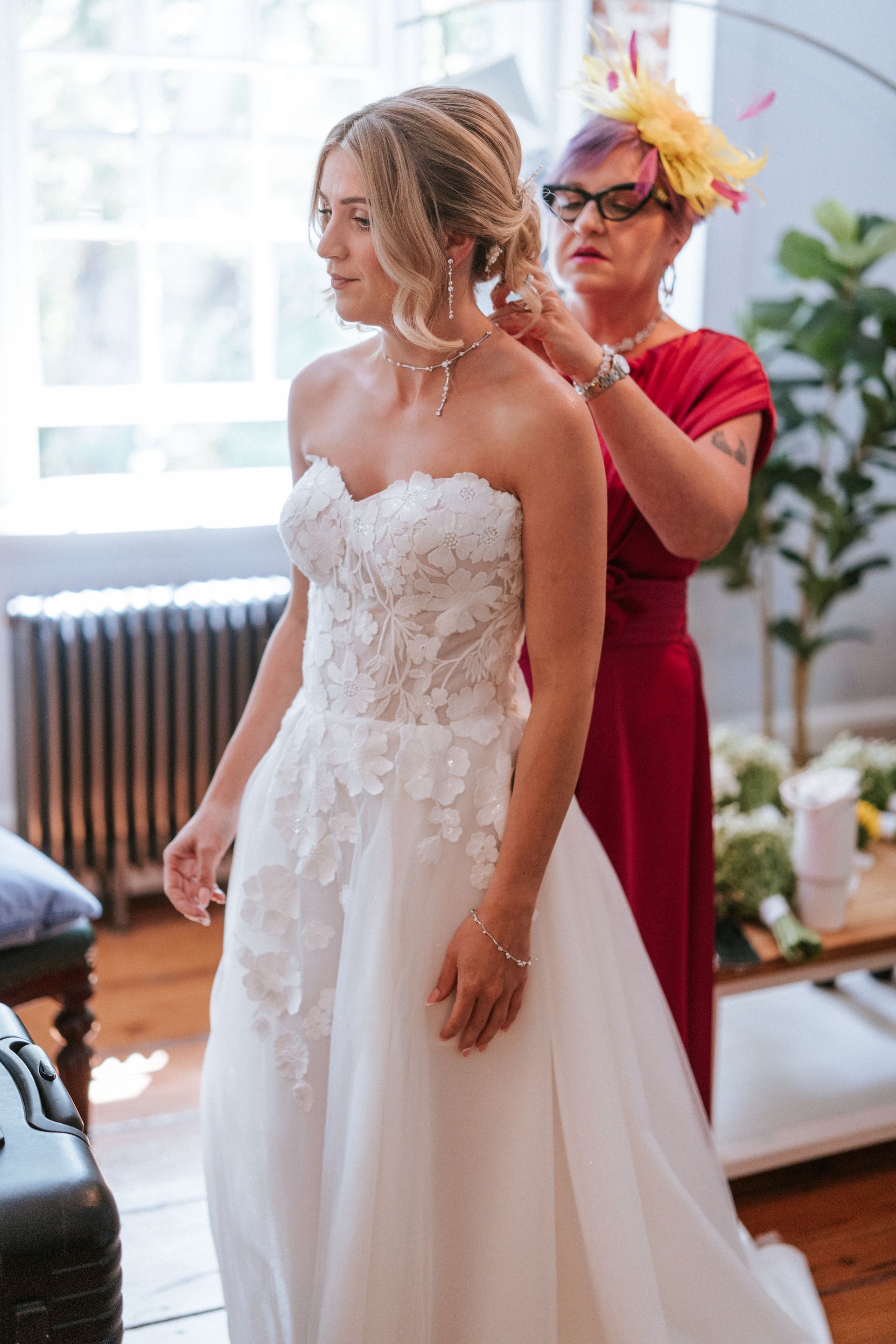 Bride in a white wedding dress being helped with her hair by a stylist in a red dress