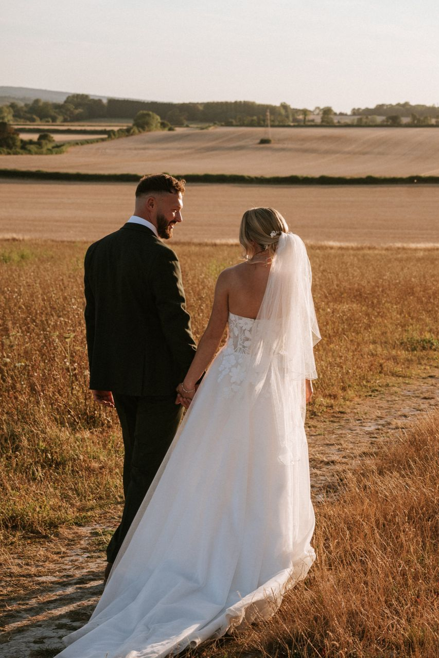 Bride and groom walking through a golden field at sunset