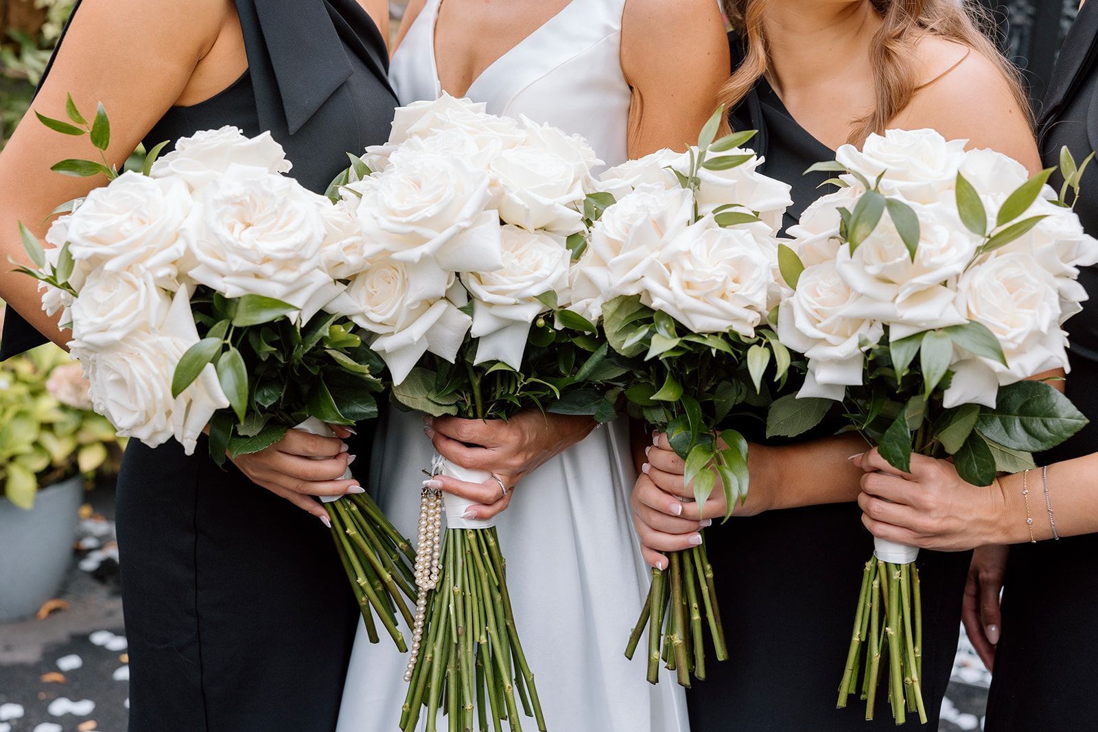 Three bridesmaids holding white rose bouquets in white dresses