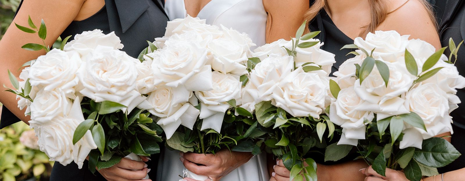 Three people holding bouquets of white flowers with greenery