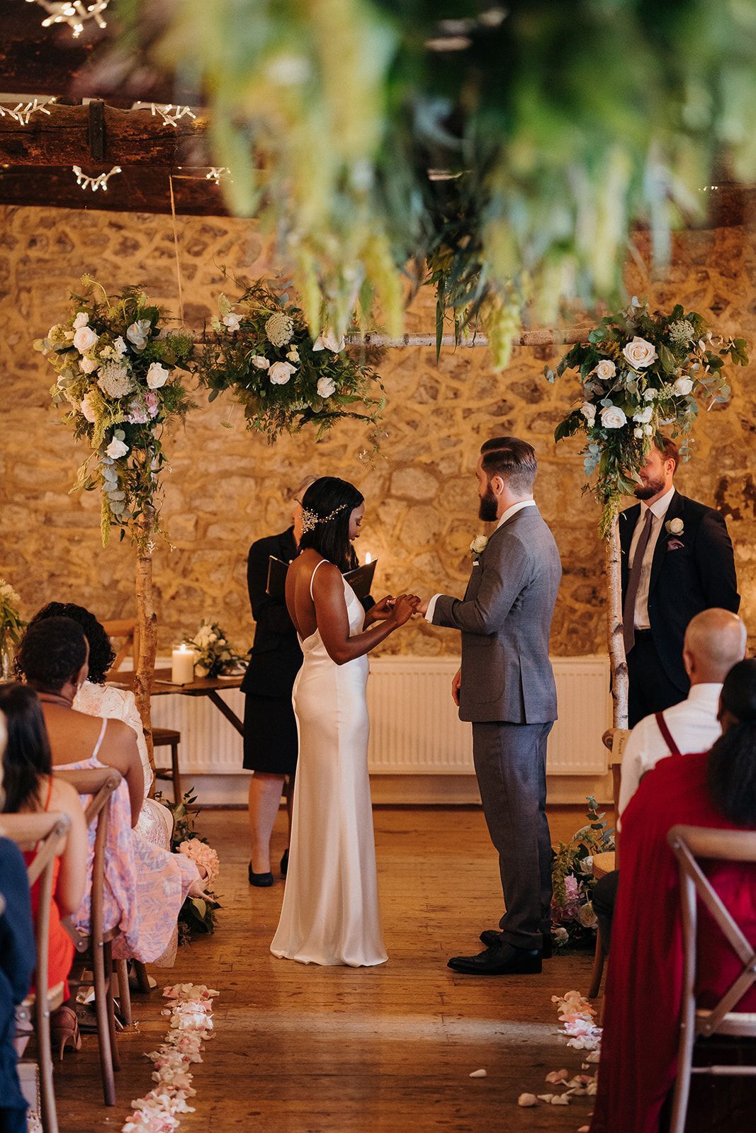 Wedding ceremony with couple exchanging vows under floral arch in a rustic indoor venue