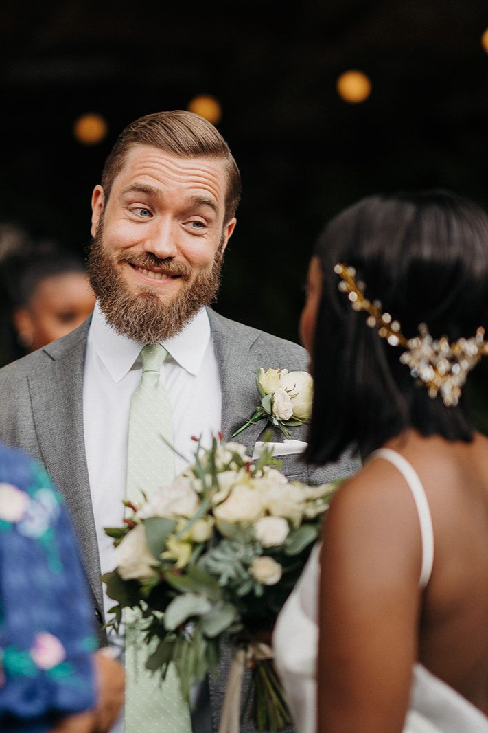 Smiling bearded man in a suit holding flowers at an outdoor wedding ceremony