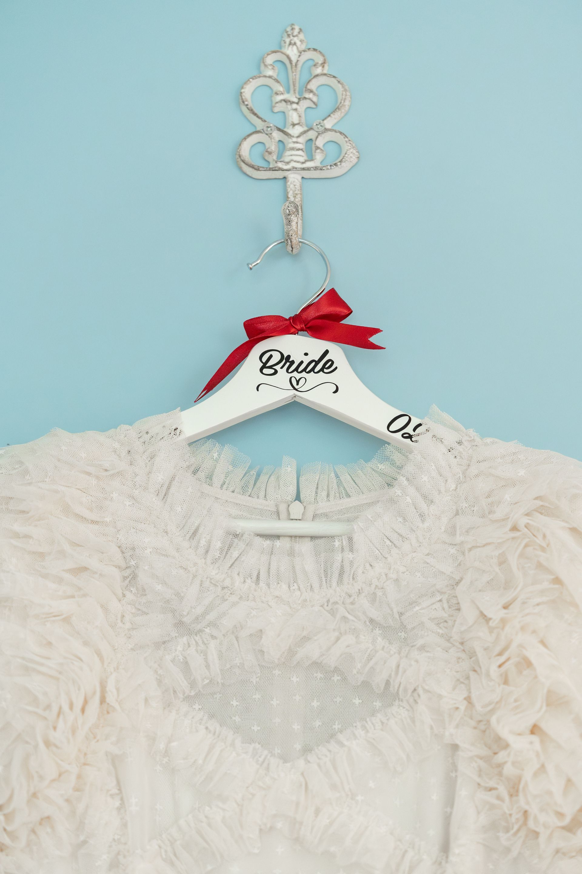 White lace bridal dress on a hanger with a red bow against a light blue wall