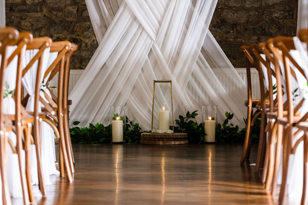 Wedding couple kissing during ceremony in a rustic barn, surrounded by smiling guests