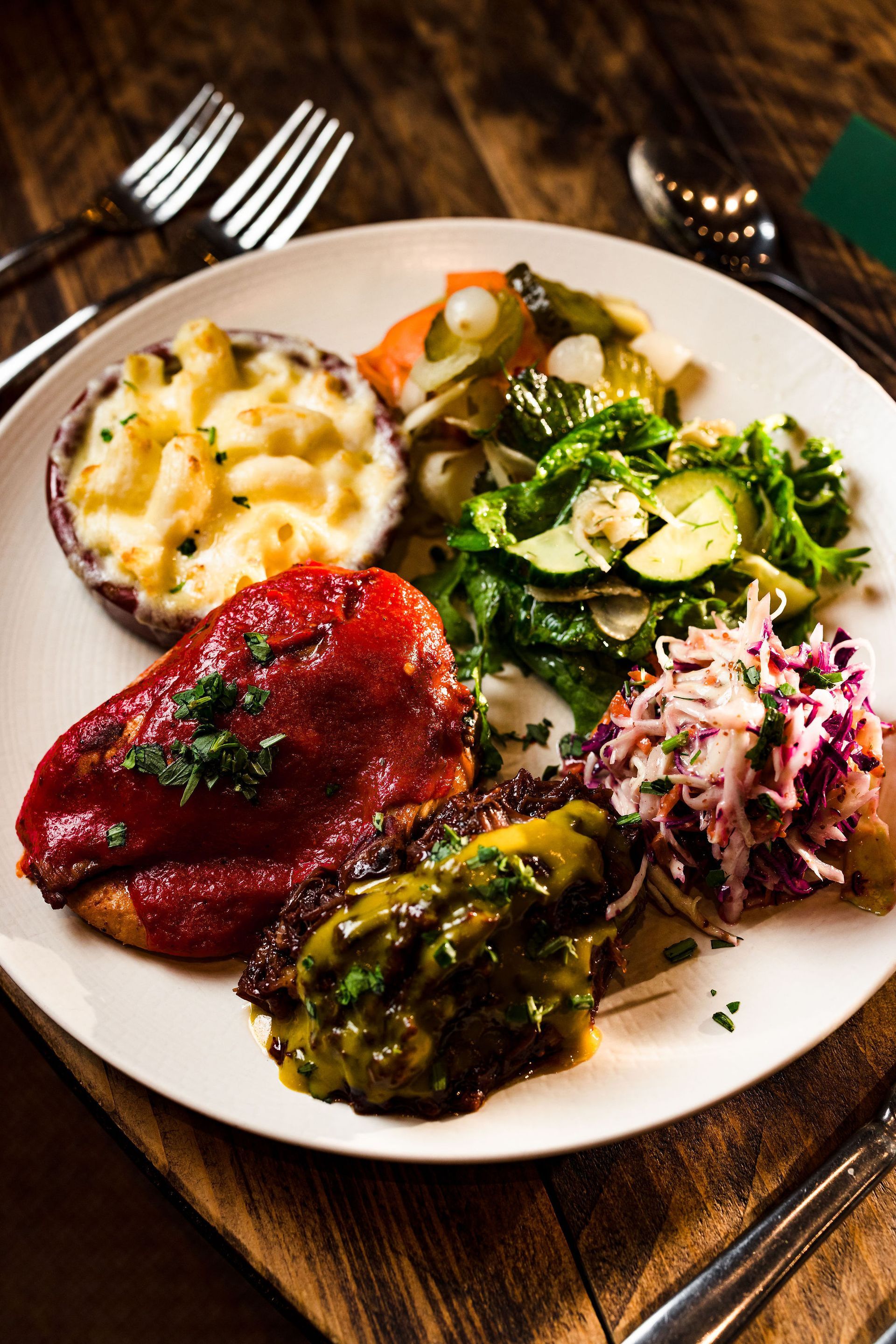 People sharing plates of food around a rustic wooden table with drinks and a centerpiece of greenery