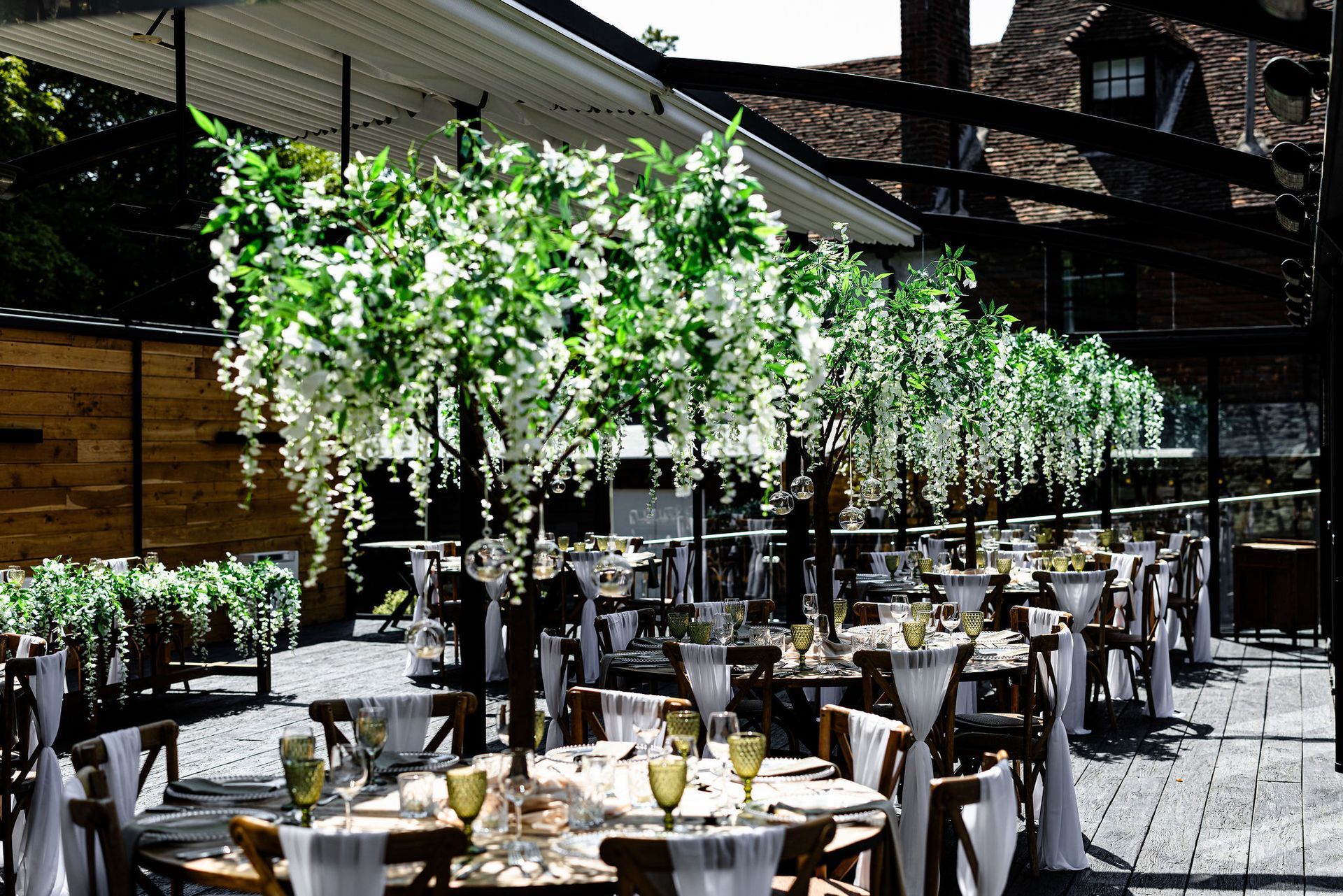 Outdoor banquet tables under hanging greenery in a sunlit patio venue