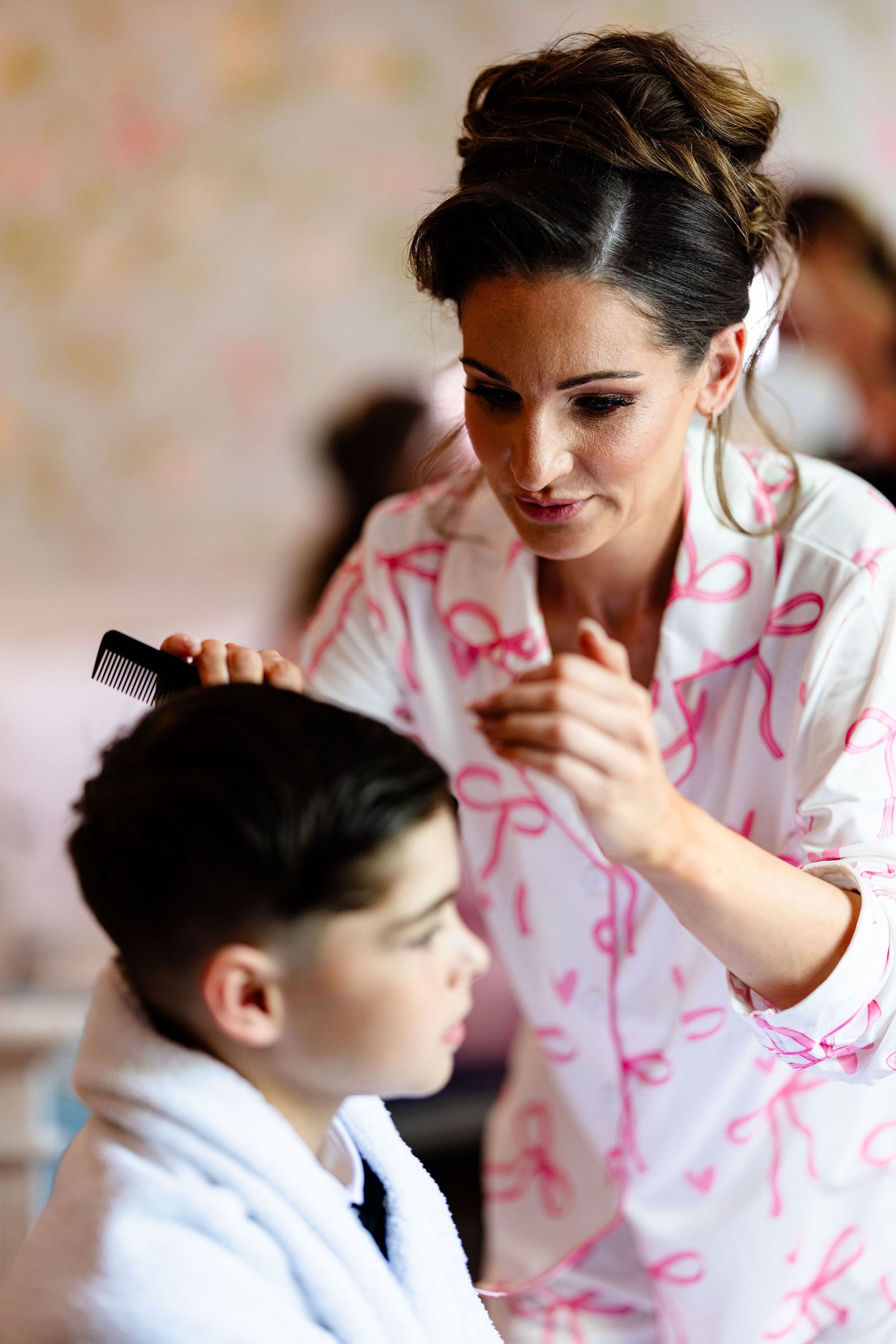 Stylist working on a seated client’s hair in a salon, with a pink robe and hairbrush visible