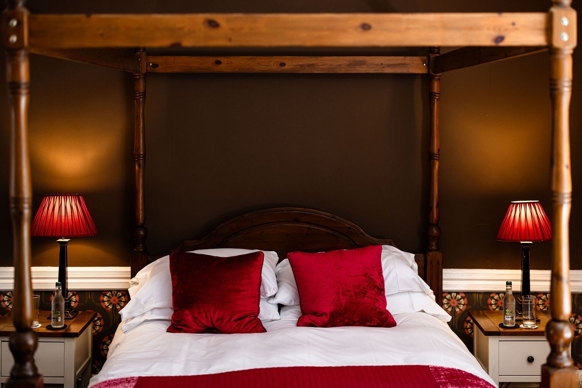 Four-poster bed with red pillows and lamps in a warmly lit bedroom