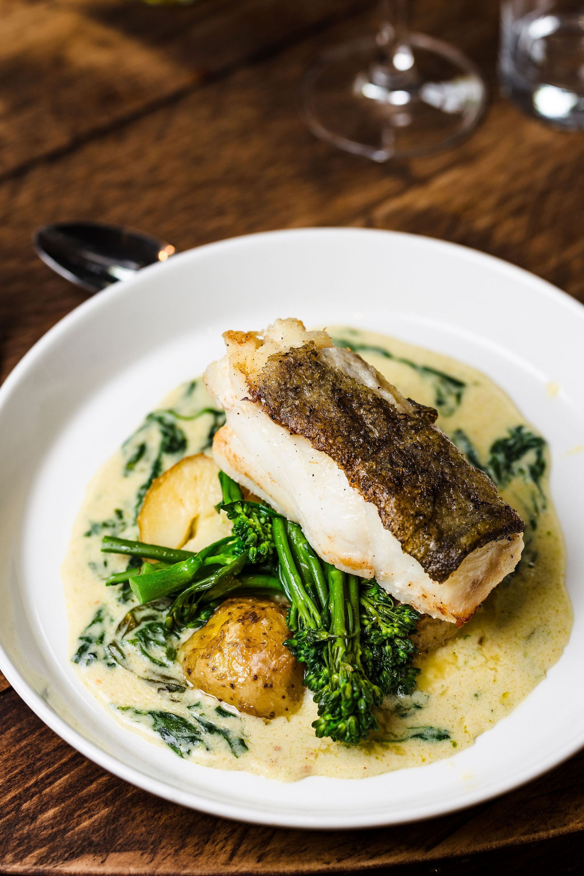 Pan-seared fish with greens in creamy sauce on a white plate on a wooden table