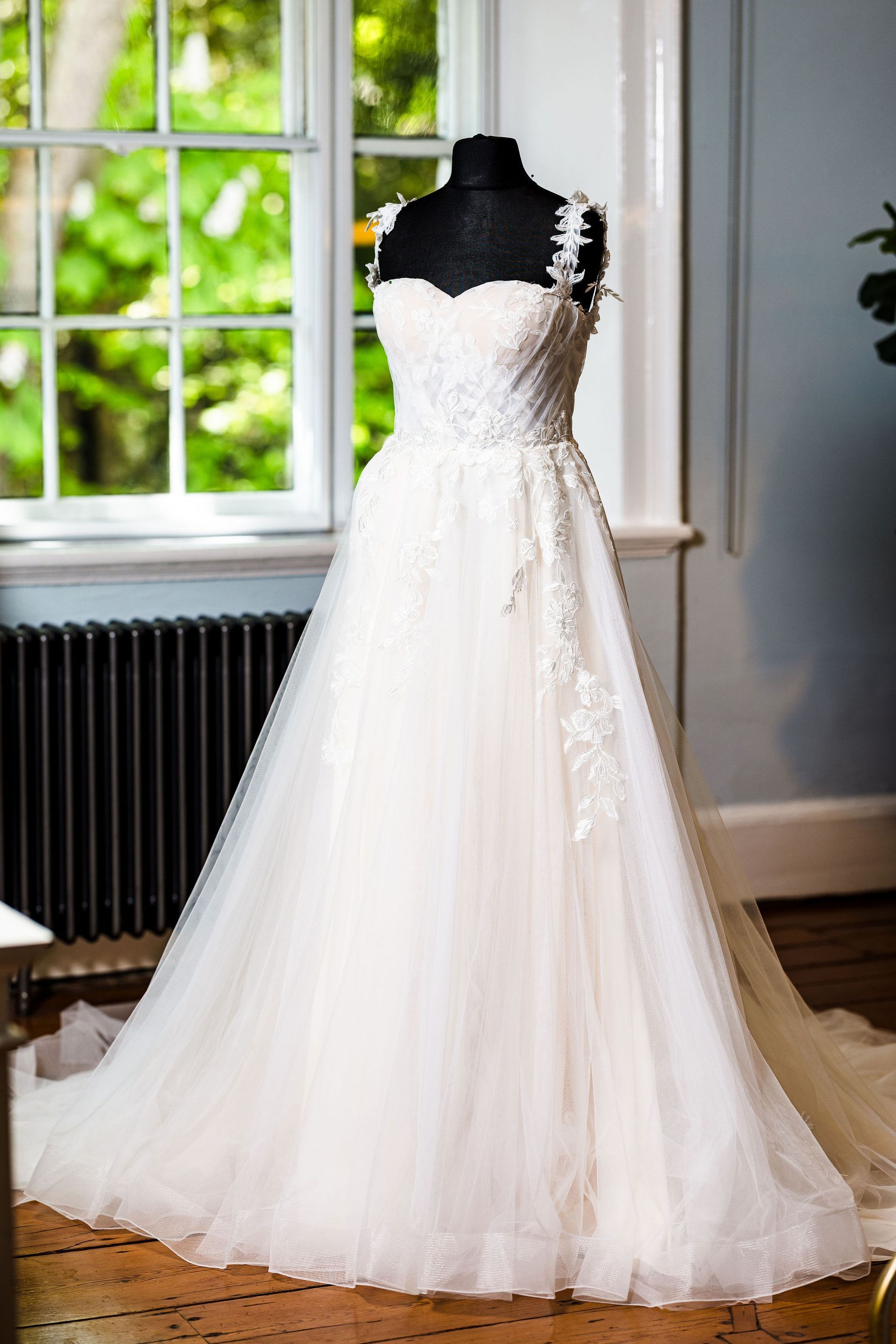 Bride adjusting her garter while sitting in a white wedding dress near a window and radiator