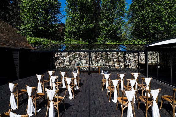 Outdoor café with seated people in a sunny courtyard beside a brick building and glass terrace.