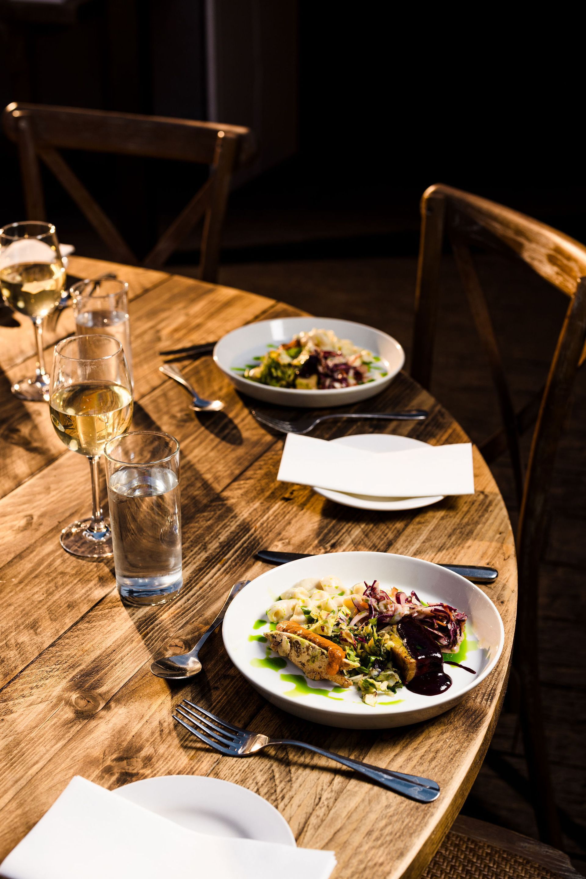 Rustic wooden table set with plates, glasses, and cutlery in a warm-lit dining setting