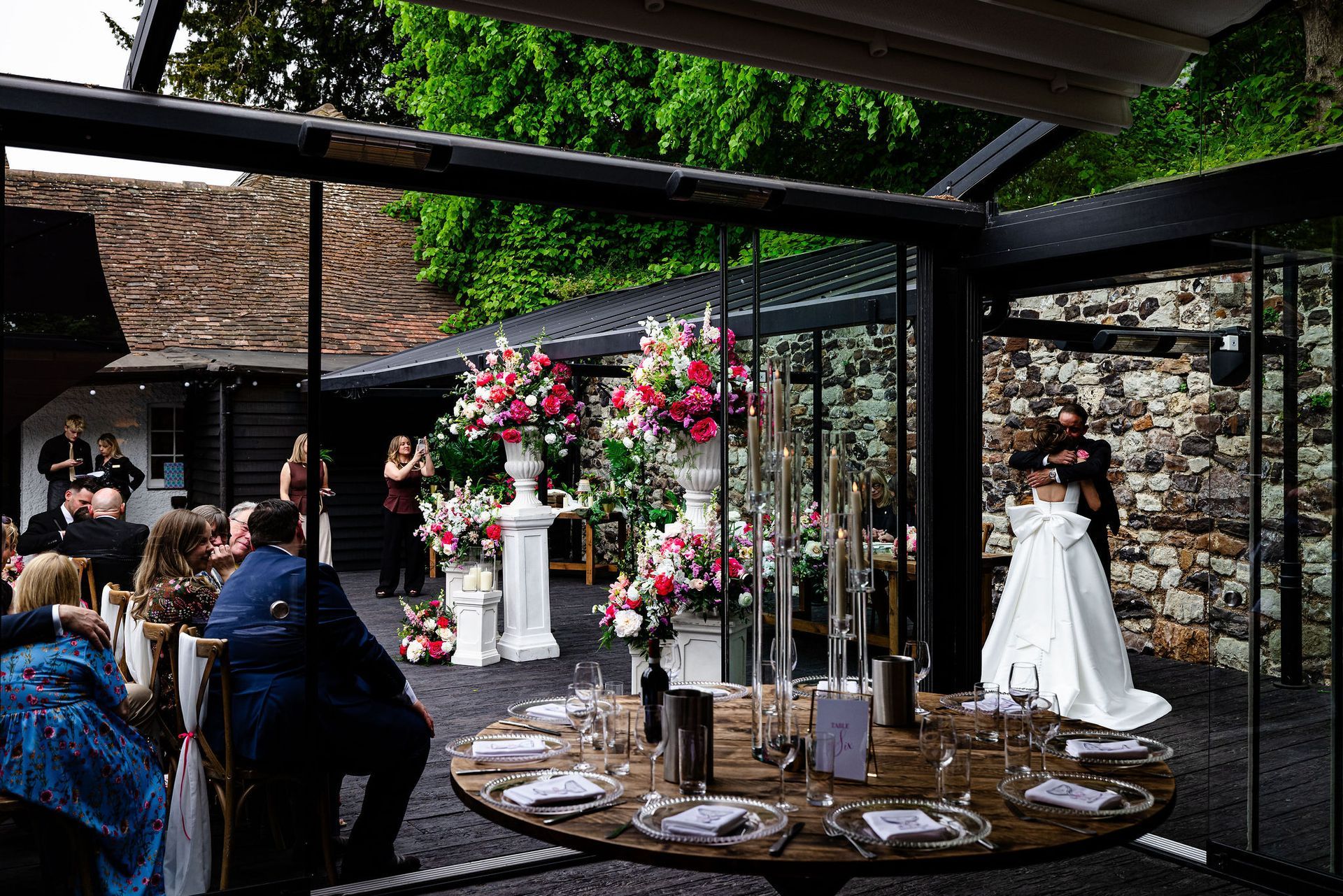 Outdoor wedding reception with floral centerpieces, decorated tables, and a white bridal dress display under a pergola