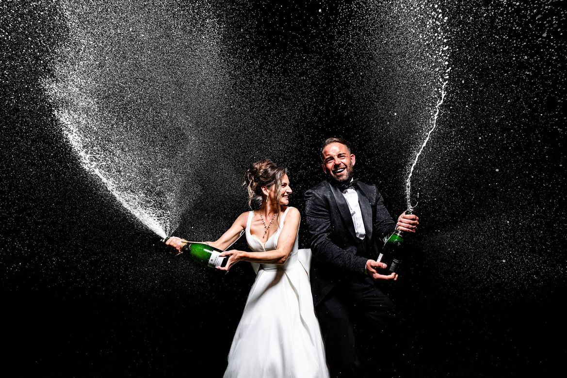 Bride and groom walk down an outdoor aisle as guests cheer and throw confetti at their wedding