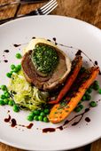 Plated gourmet dish with beef medallion, carrots, peas, and greens drizzled with sauce