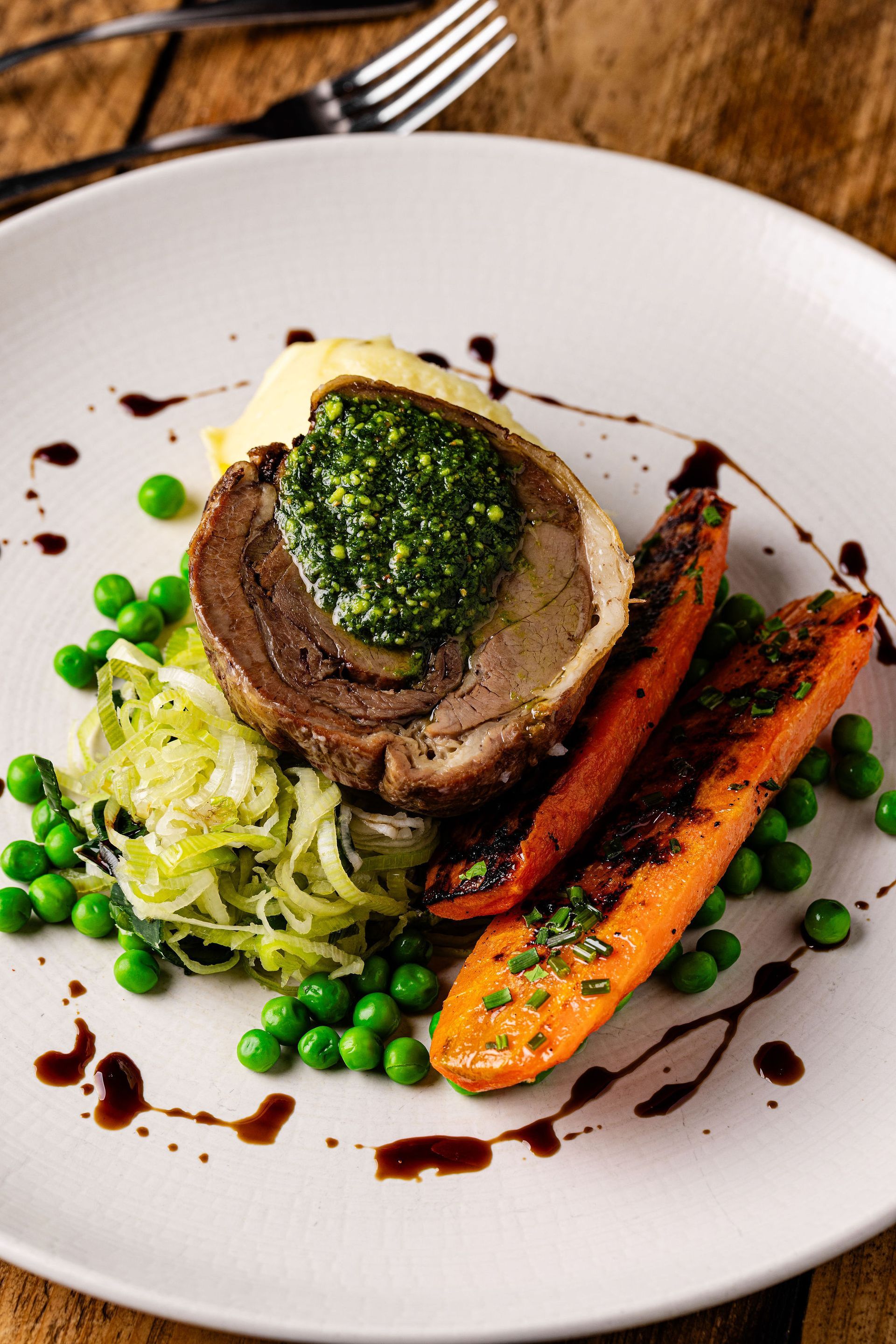 Plated gourmet dish with beef medallion, carrots, peas, and greens drizzled with sauce