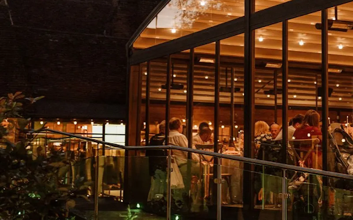Romantic twilight wedding reception glowing inside a modern glasshouse with a domed roof.