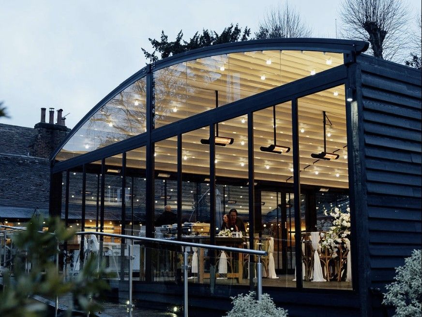 Modern glass-fronted restaurant building at dusk with warm interior lights and a curved roof