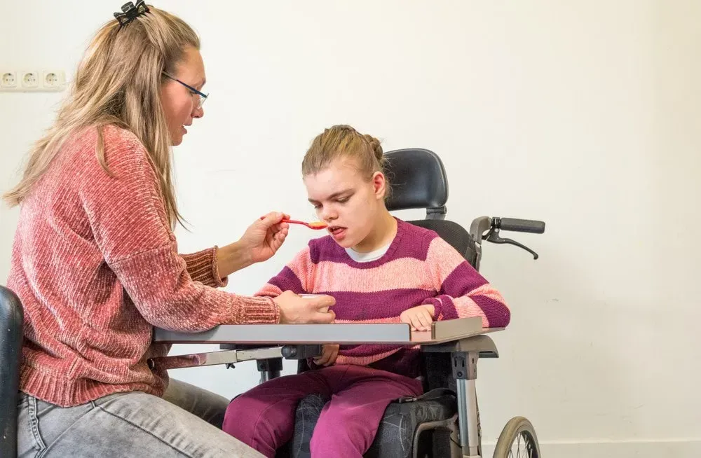 A Person in a Pink Sweater Feeds a Child — CQ Home Care in Yeppoon, QLD