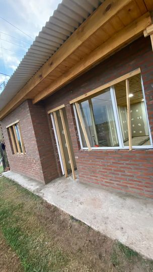 Exterior de una casa de ladrillo con ventanas de marcos blancos y un techo de chapa ondulada