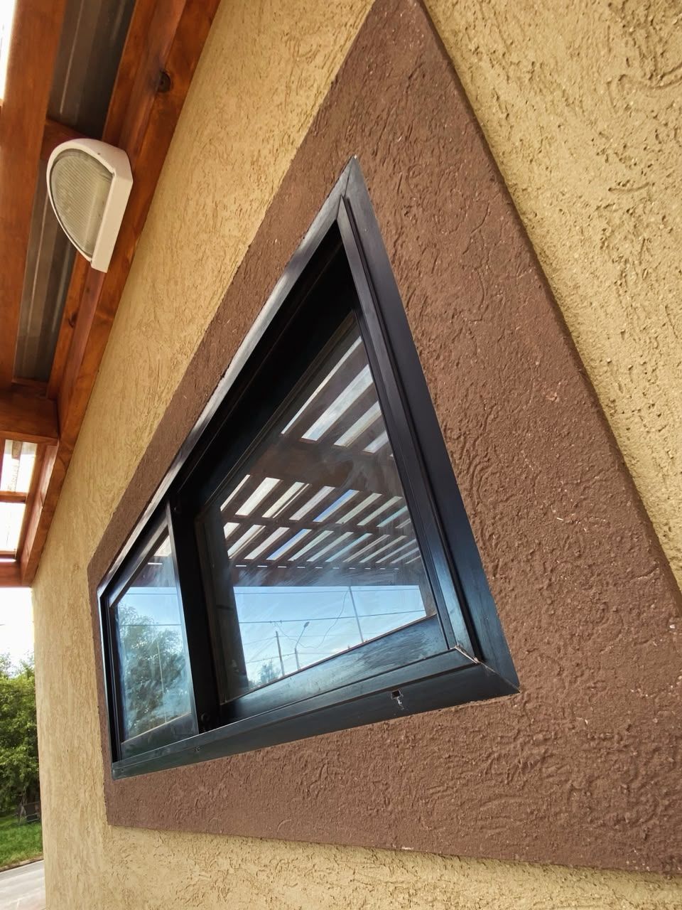 Pequeña ventana con marco negro, situada en una pared exterior de color marrón y beige, vista desde un ángulo.
