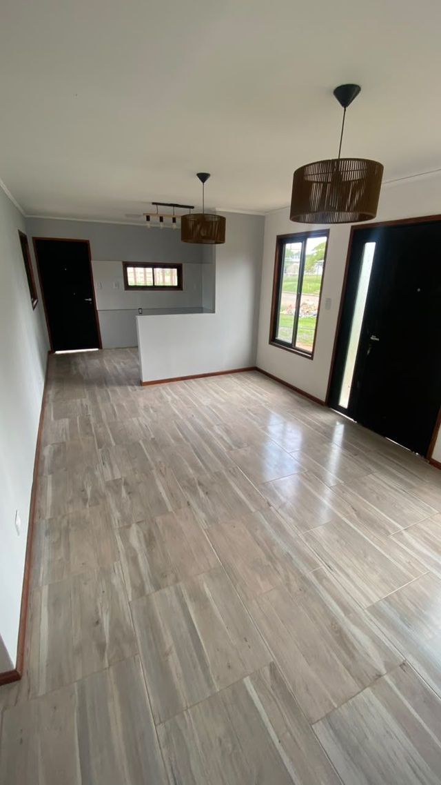 Habitación moderna vacía con suelos de madera clara, paredes blancas, lámparas colgantes, ventana y puerta oscura.