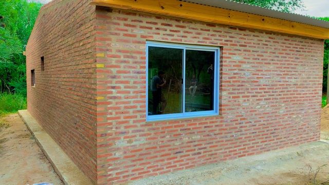 Pequeña casa de ladrillo con una ventana y un camino de hormigón, vista desde el lateral.