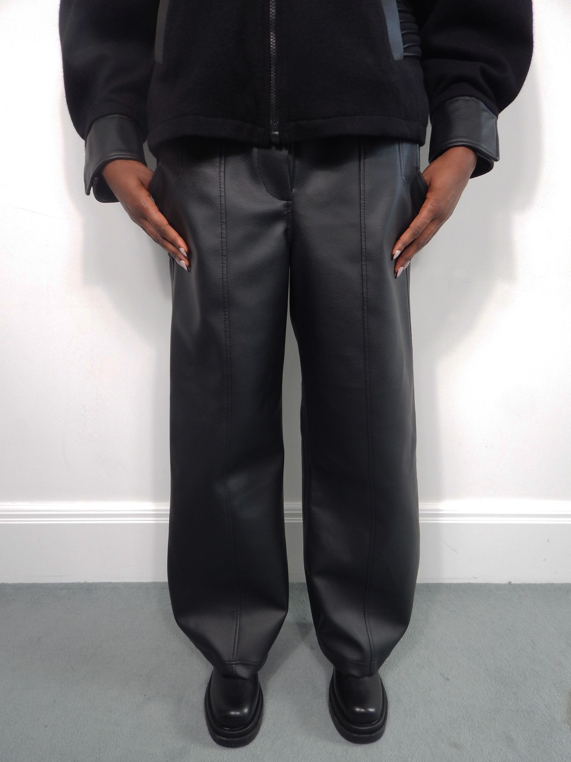 Person wearing a black jacket and leather-look pants, standing indoors.