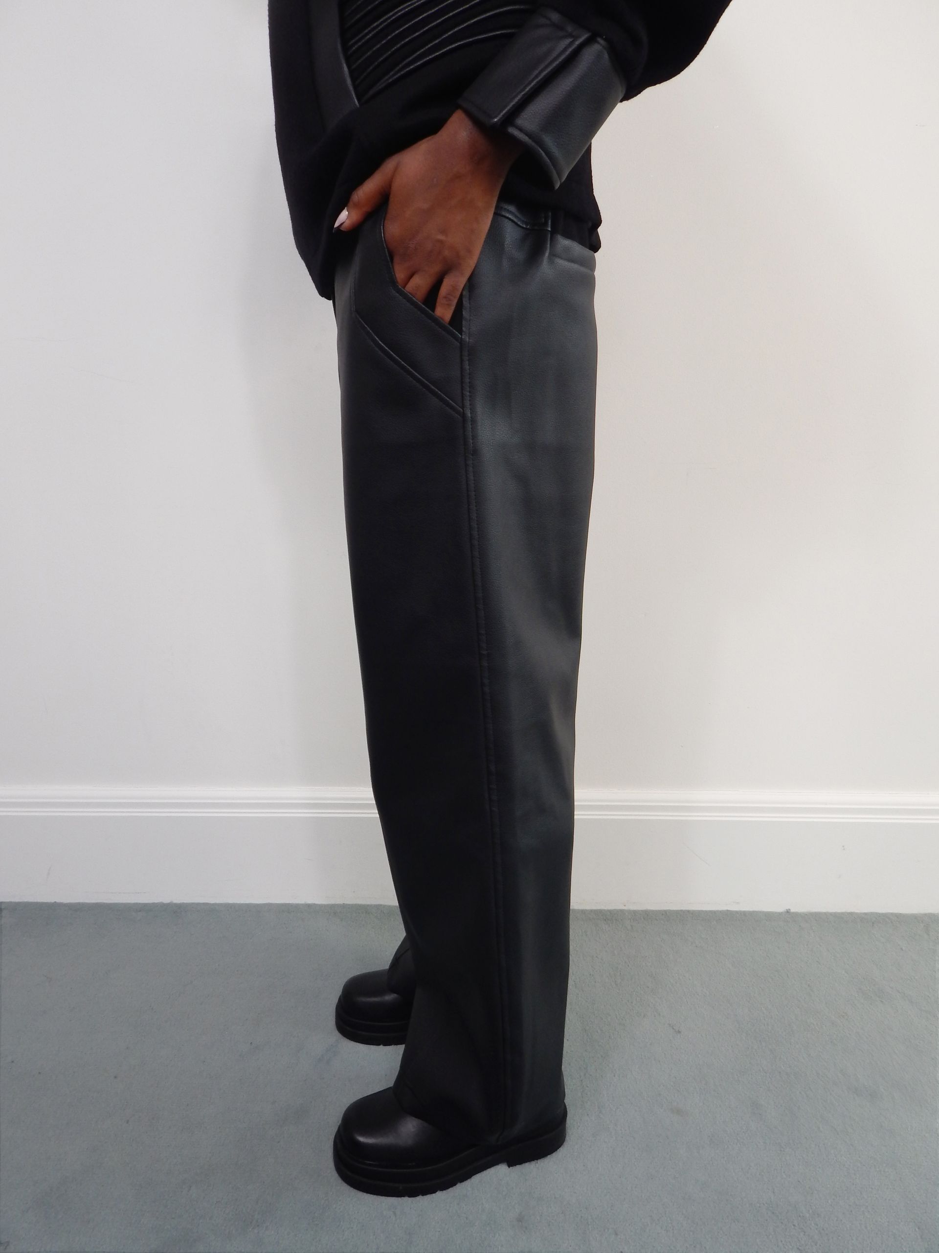 Person wearing a black jacket and leather-look pants, standing indoors.