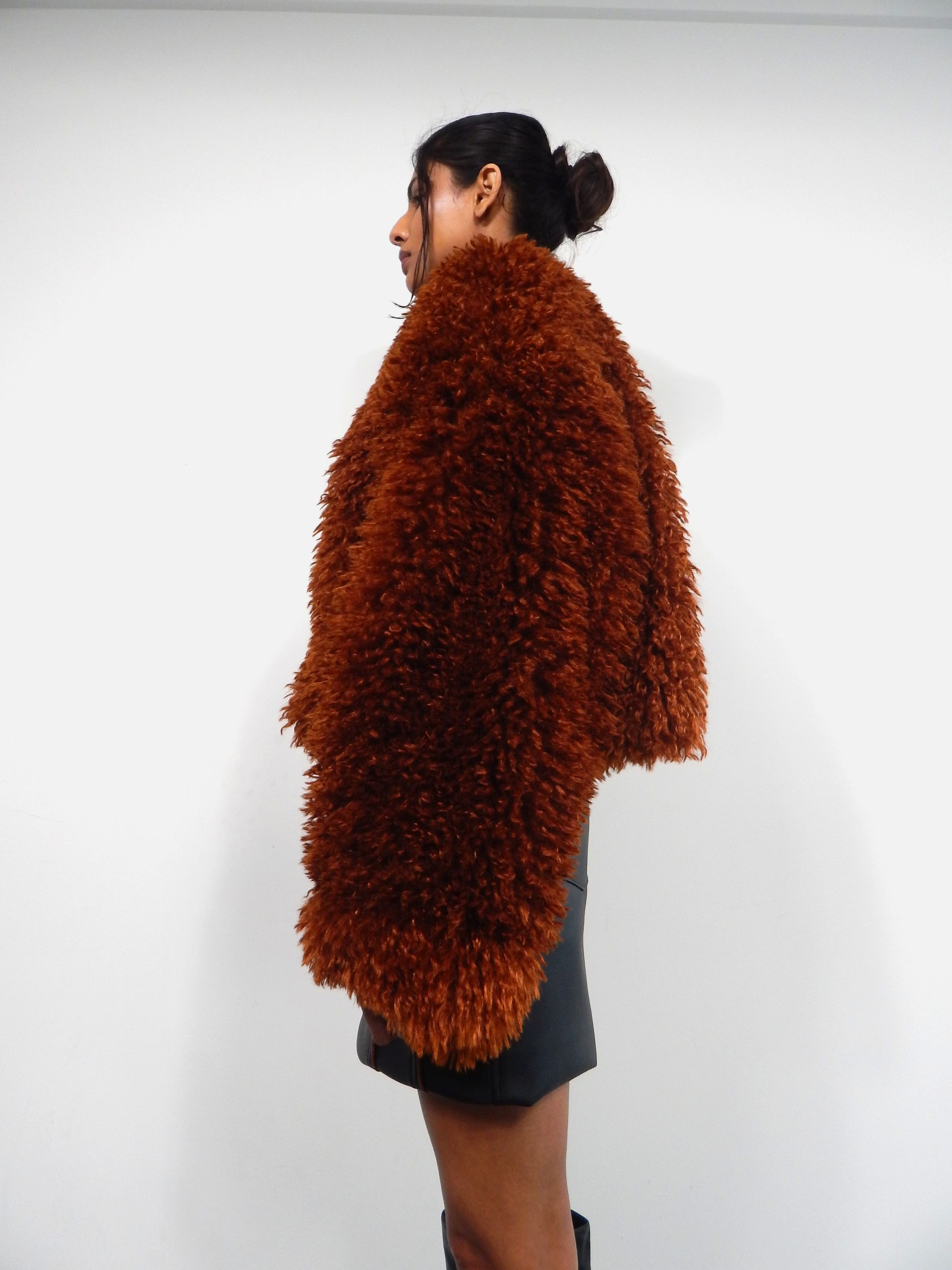 Woman in a brown furry jacket, black skirt, and a neutral setting.