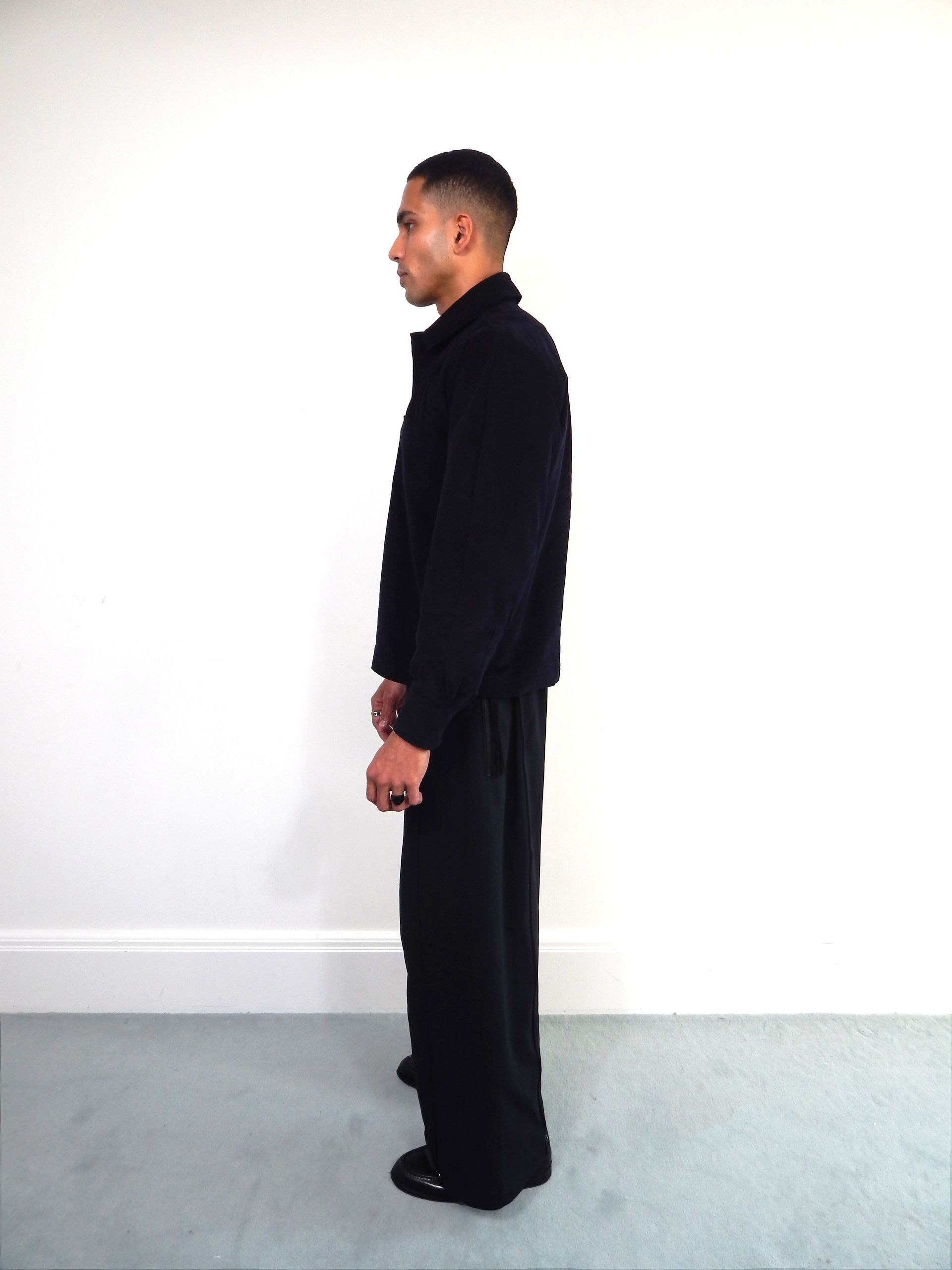 Person in black sweater and pants, standing against a white wall.