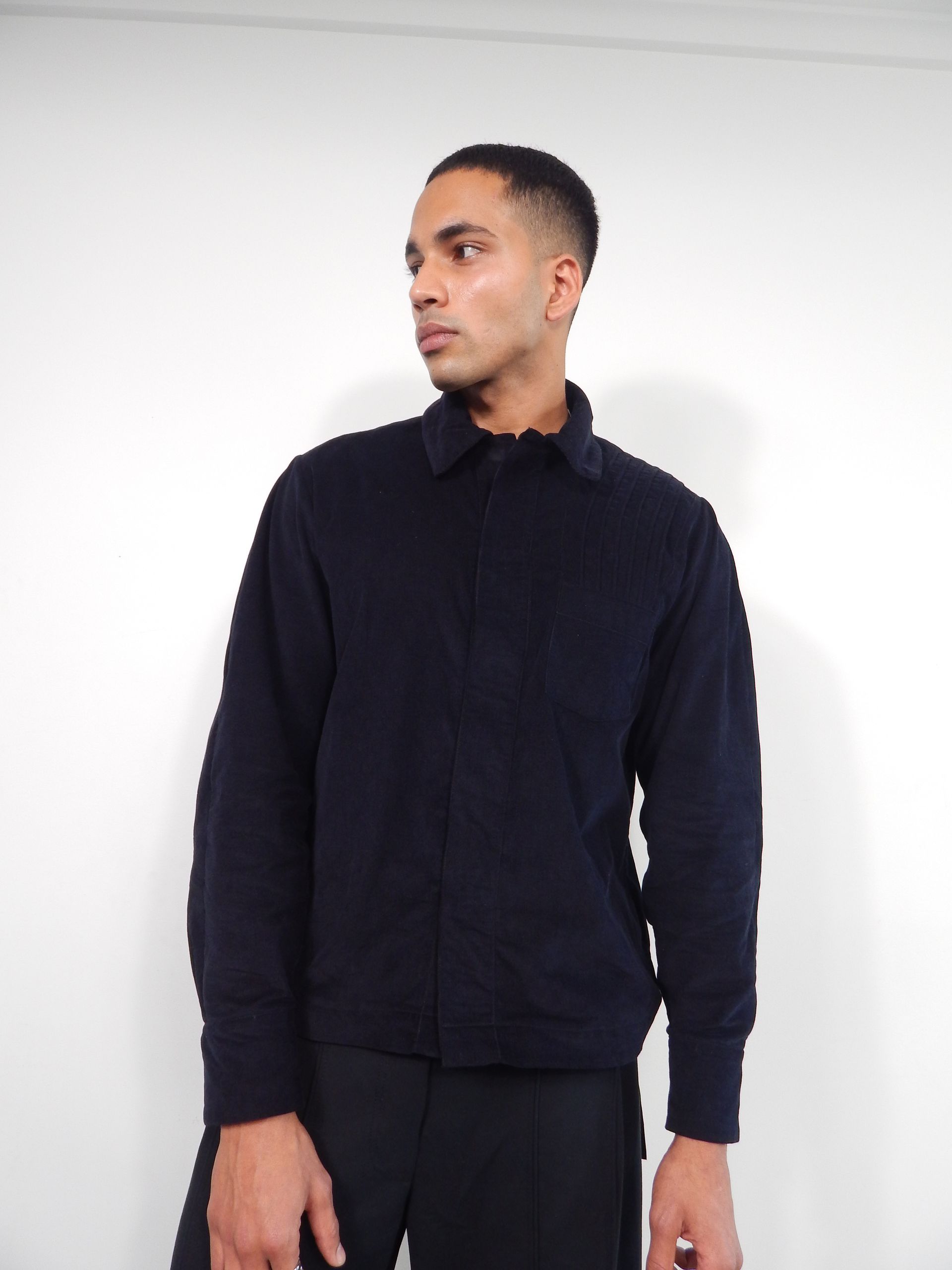 Man in dark blue jacket and pants, looking to the side, against a white backdrop.