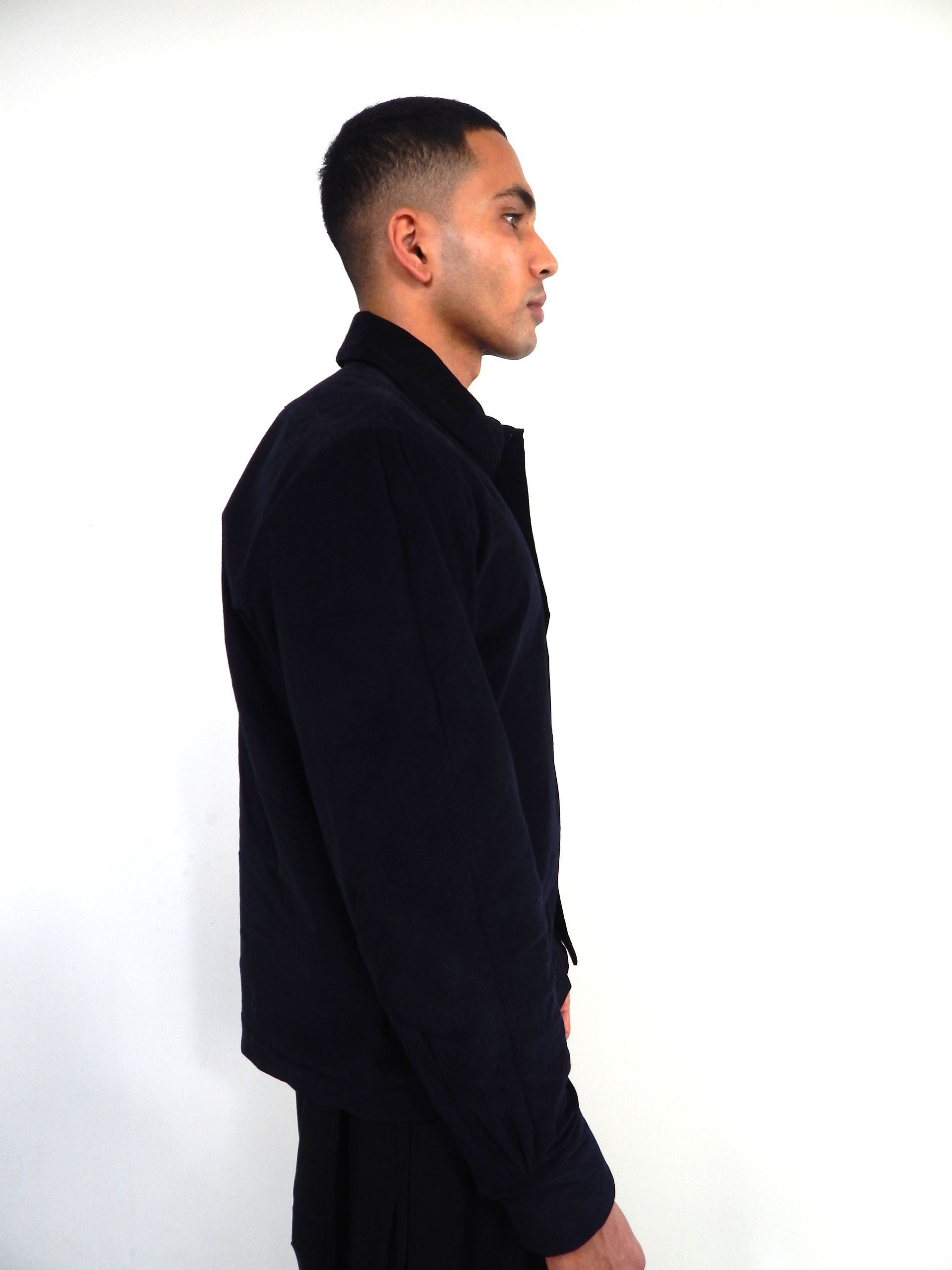 Man in dark blue jacket and pants, looking to the side, against a white backdrop.
