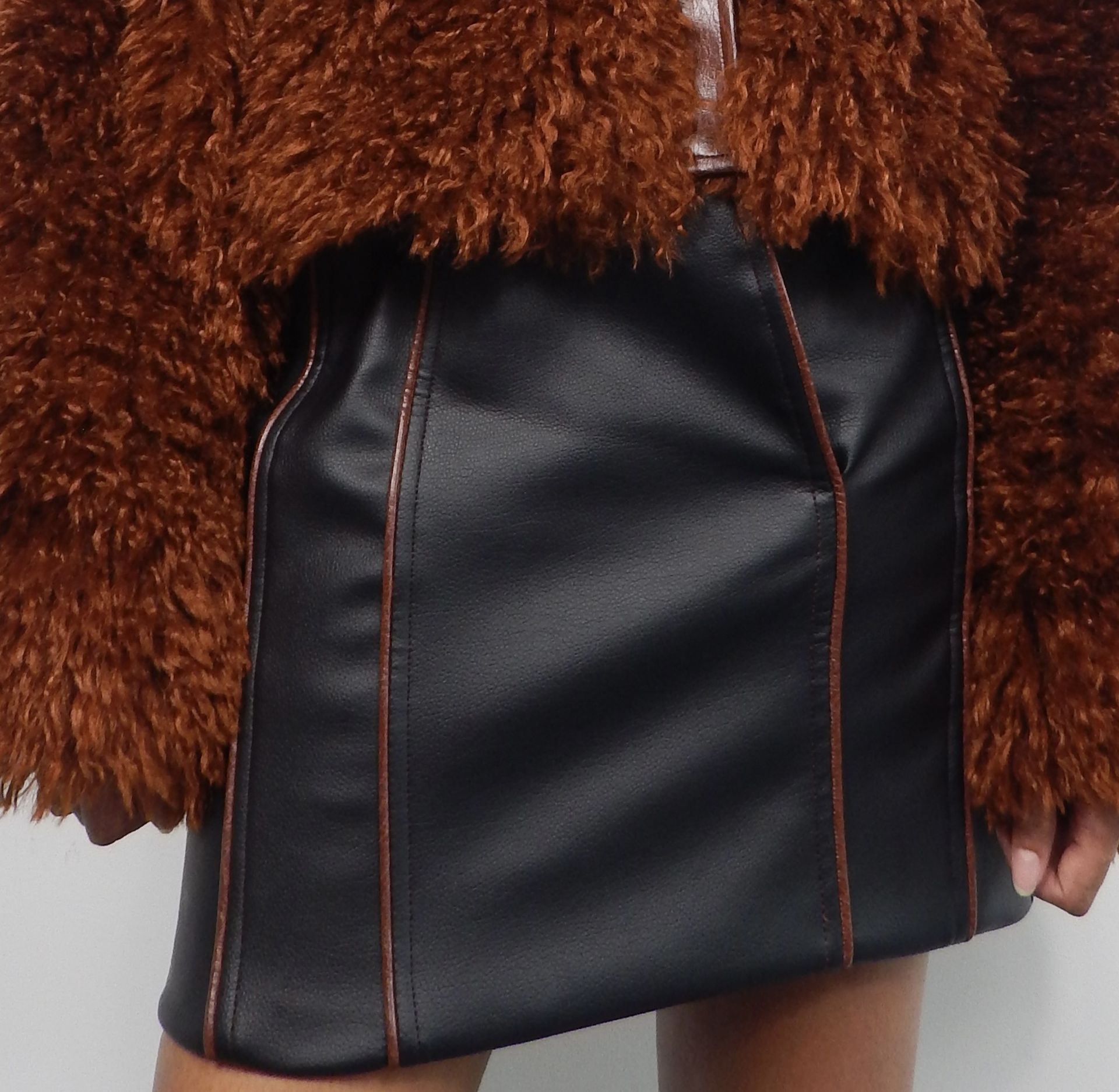 Cropped view of person in a fuzzy brown jacket and black skirt. The skirt has visible stitching.