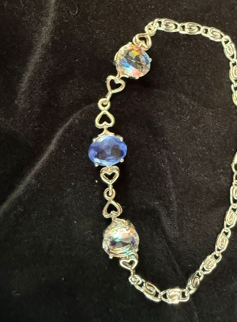 A silver bracelet with blue stones and hearts on a black cloth