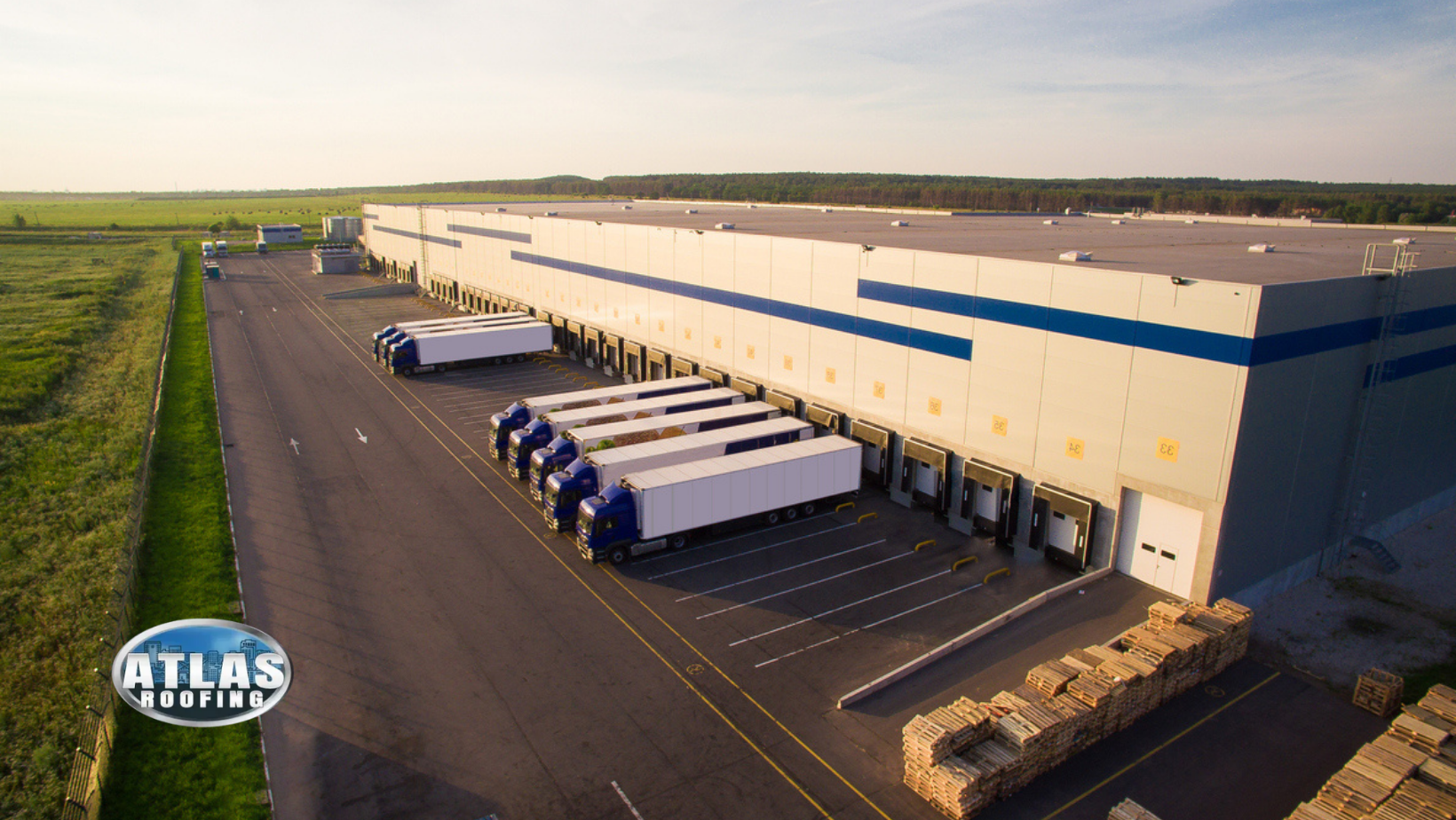 Trucks loading at a large warehouse. Light blue and white building, parked trucks, and a grassy field.