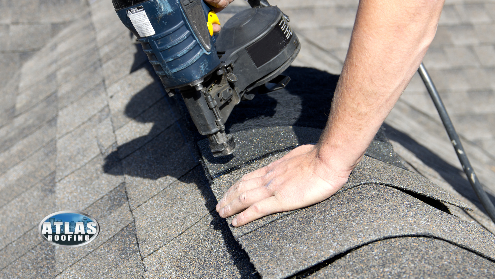 Person using a nail gun to attach roofing shingles on a roof.