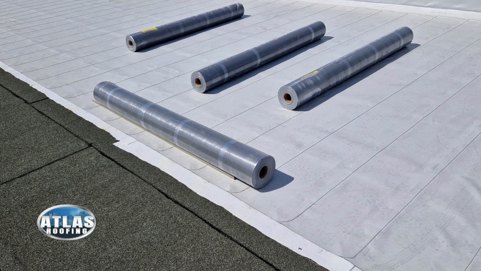 Several rolls of roofing material on a white roof surface, with a green edge.