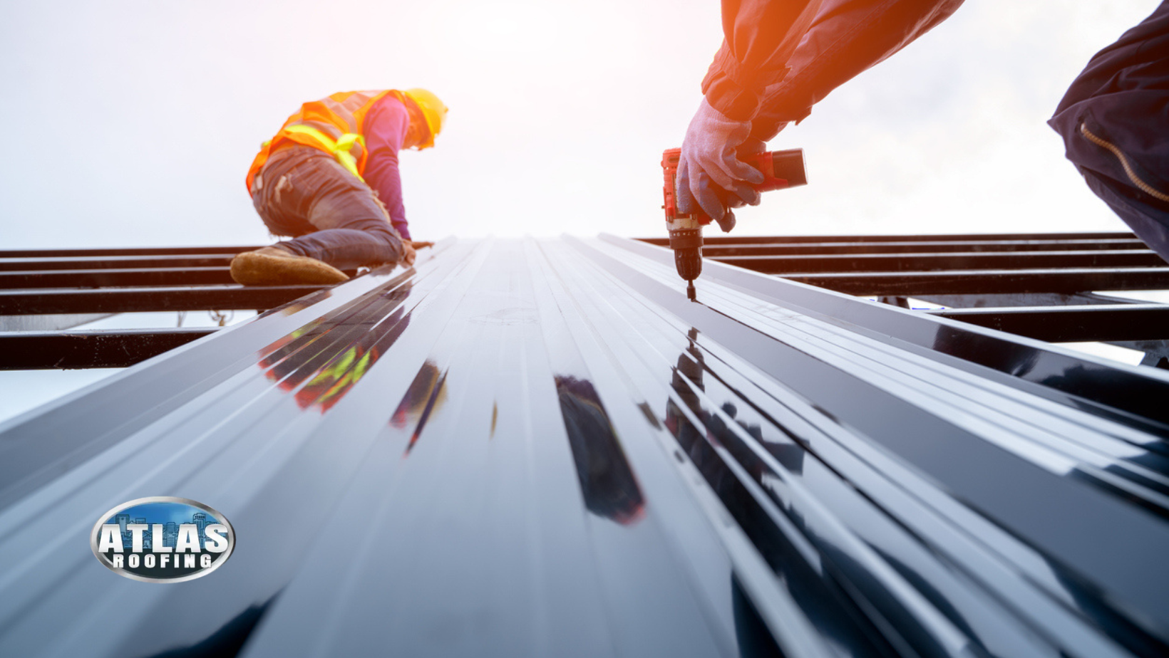 Two workers installing a metal roof; one drills, the other kneels; bright sunlight.