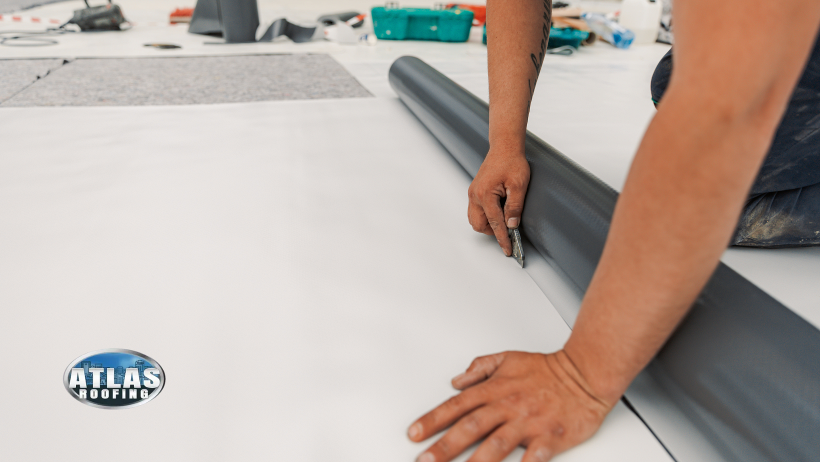 Person cutting dark rolled material with a utility knife on a white surface.