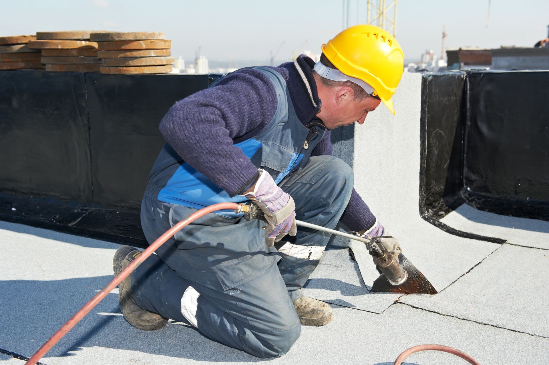 A man wearing a hard hat is working on a roof with a torch.