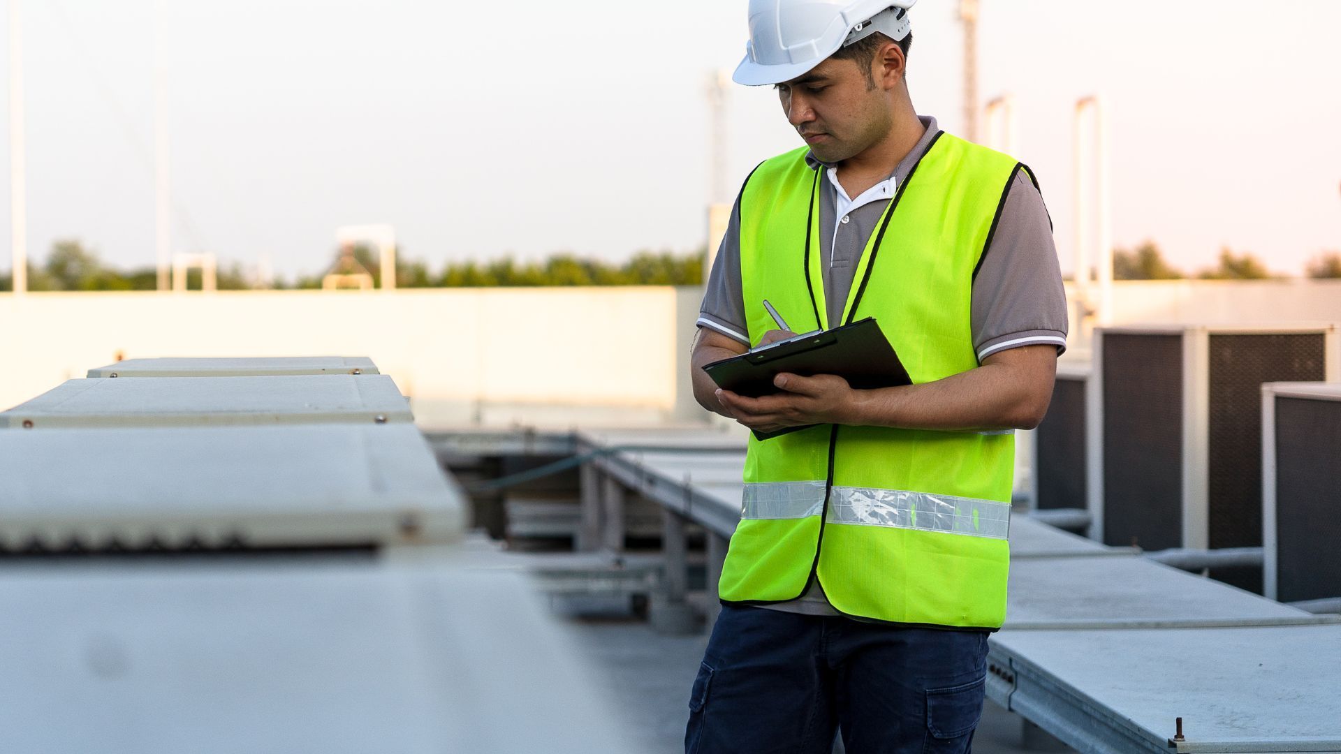 A man in a yellow vest and hard hat is holding a clipboard.